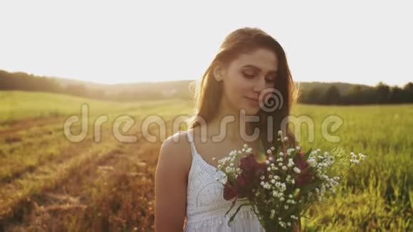 夏天的傍晚一位美丽的年轻女子在草地上开着一束野花头发随风飘荡视频的预览图