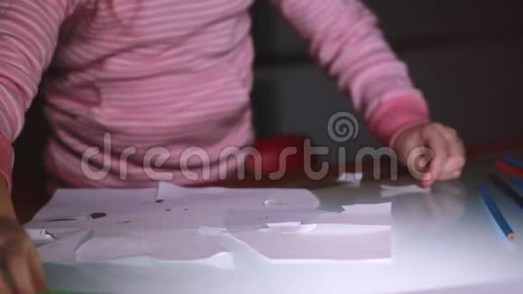 小女孩的特写镜头她的手穿着粉红色的毛衣用剪刀在玻璃桌上剪纸片形状视频的预览图