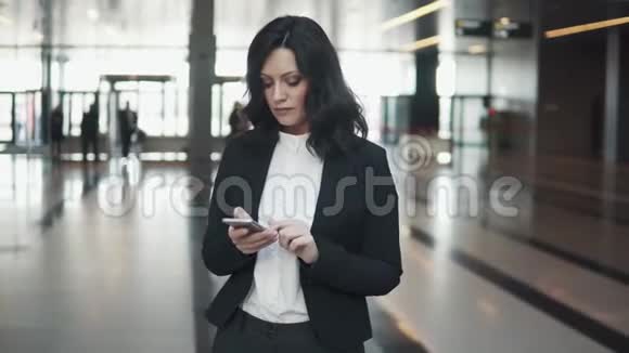年轻的商务女性站在现代办公楼的大厅里使用智能手机视频的预览图