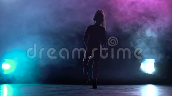 女孩站在一个黑暗的工作室抬起她的腿多色烟雾背景剪影后面的光视频的预览图