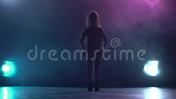 小女孩坐在工作室的绳子上多色烟雾背景剪影后面的光视频的预览图