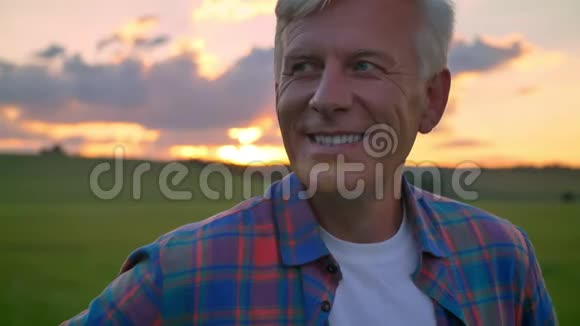 英俊的老人微笑着看着摄像机站在麦田上美丽的景色与夕阳在视频的预览图