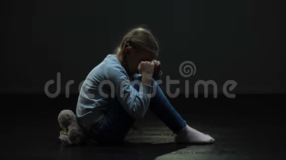 心烦意乱的小女孩带着泰迪熊在黑暗的废弃房间里哭泣孤独视频的预览图