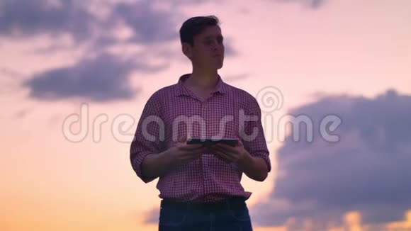 年轻的帅哥在平板电脑上打字环顾四周背景是美丽的粉红色天空视频的预览图