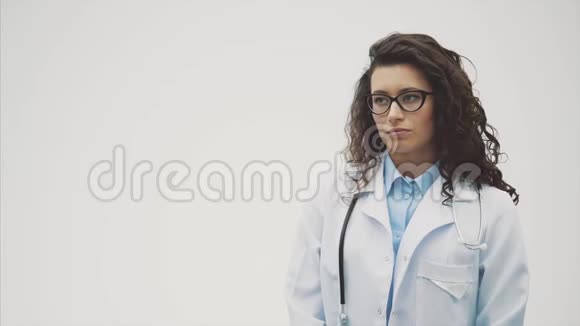 年轻漂亮的黑发医生灰色背景穿着统一的医疗制服在灰色背景下受苦视频的预览图