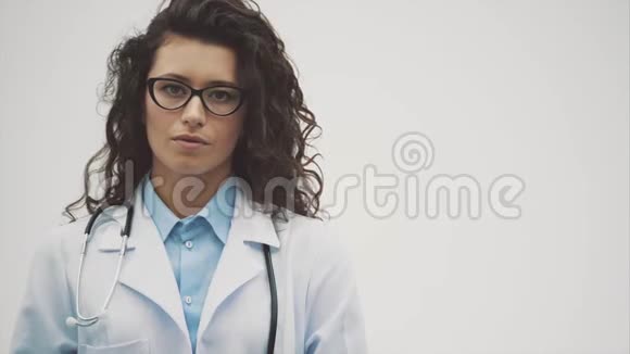 年轻漂亮的黑发医生灰色背景穿着统一的医疗制服在灰色背景下受苦视频的预览图