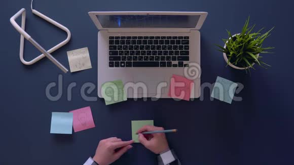 一个穿灰色衬衫的有创意的女人坐在桌子旁在贴纸上发明和写商业想法空中射击视频的预览图