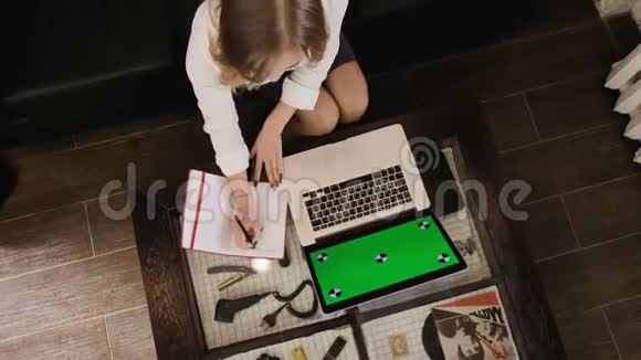 一个金发女孩带着一台笔记本电脑她在笔记本上工作并做笔记木制内部绿色笔记本电脑视频的预览图