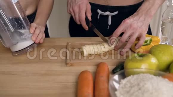 在厨房里的搅拌机里男人的手切香蕉和女人的手混合牛奶视频的预览图