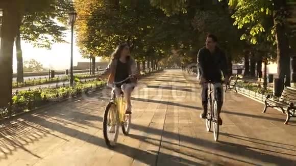 夏季在城市公园或林荫大道上骑自行车的年轻快乐夫妇或朋友的正面景色人民视频的预览图