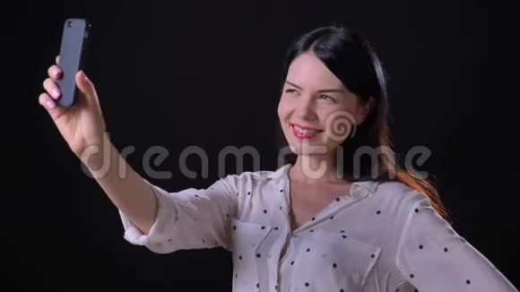 迷人的可爱的年轻女子自拍和微笑的电话相机孤立在黑色工作室背景视频的预览图