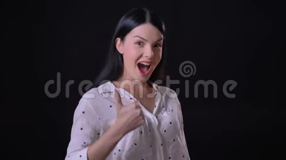 迷人的快乐的黑发女人竖起大拇指对着镜头欢呼在黑色的背景下与世隔绝视频的预览图