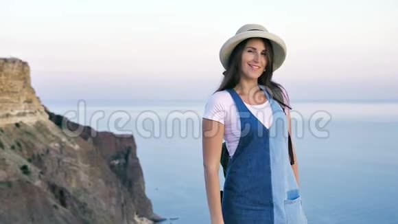 美丽优雅的年轻女子戴着帽子在夕阳下欣赏壮丽的大海和群山视频的预览图