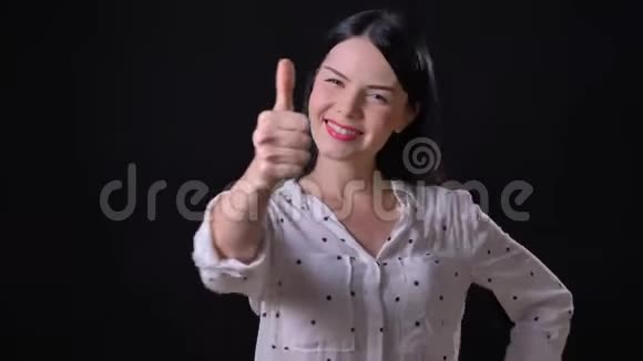 美丽的年轻女子在镜头前竖起大拇指微笑着孤独地站在黑色的背景上视频的预览图