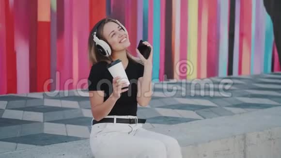 一位迷人的女孩在户外用耳机听音乐的肖像视频的预览图