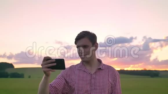 英俊的年轻人自拍看着相机站在麦田上背景是美丽的粉红色天空视频的预览图