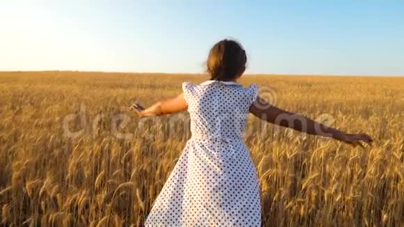快乐的女孩在成熟的麦子里在蓝天上跳舞慢动作视频的预览图