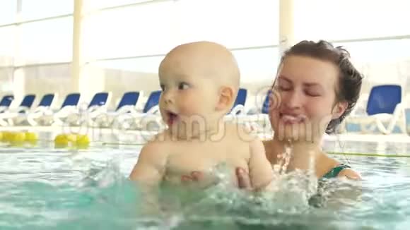 可爱的婴儿抱着妈妈正在游泳池里学习游泳这孩子把手溅在水上视频的预览图