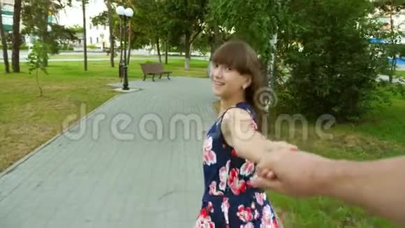 女孩和男人一起跑过手臂微笑着回头看着他在晚上的公园里笑慢动作视频的预览图