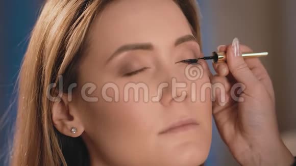 化妆师用黑色眼线在一个白种人金发女郎的脸上用专业的刷子涂在眼睑上视频的预览图