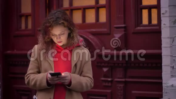 年轻的金发白种女孩在模糊的夜市背景下专注地看着智能手机视频的预览图
