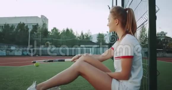特写职业网球女孩坐在网球场的草地上用球拍敲打网球视频的预览图