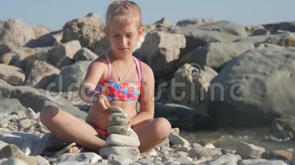 小女孩在海边的海滩上建了一座鹅卵石塔孩子梦想的概念视频的预览图