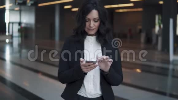 年轻的商务女性站在现代办公楼的大厅里使用智能手机视频的预览图