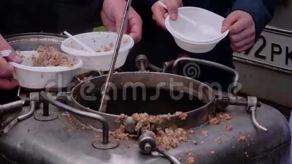 厨师把一个大锅炉里的粥放在人们手中的塑料盘子里现场厨房的特写视频的预览图