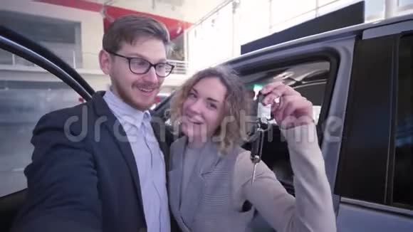 消费者夫妇带着钥匙在汽车经销商新购车辆附近的手机上拍照视频的预览图