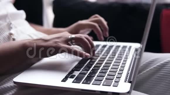 一个年轻女性手在银色笔记本电脑上打字的目标镜头电脑在她腿上黑色屏幕视频的预览图