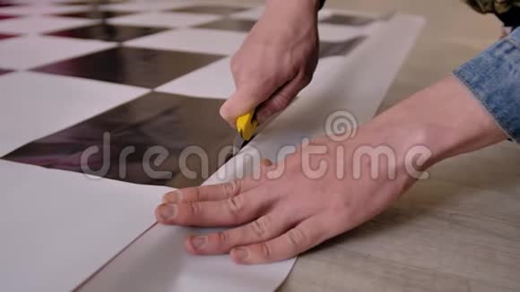 一个人用一只手拿着一把文具刀切一块帆布特写双手帆布在地板上视频的预览图