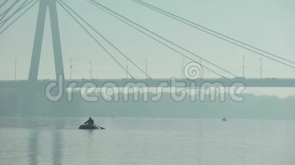 乘坐充气船在大桥下航行的渔夫雾蒙蒙的天气大城市视频的预览图