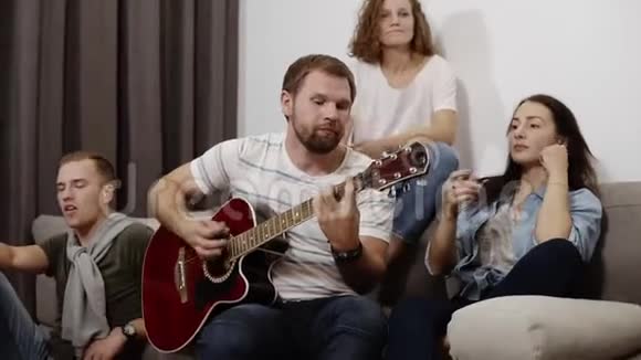 快乐的朋友坐在沙发上听着家伙唱歌弹吉他一起玩得开心视频的预览图