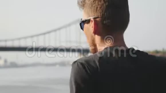 活泼的运动员沿着河跑年轻的肌肉男在桥附近跑步强壮苗条的男孩在城市码头慢跑视频的预览图