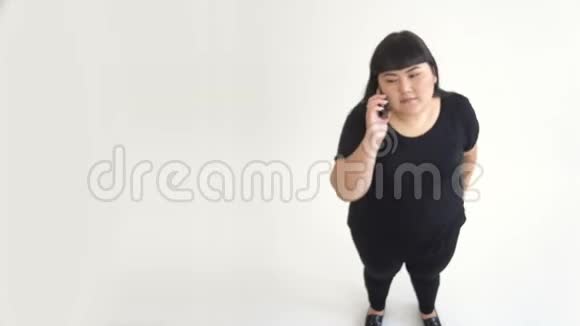 一位20岁的胖美亚洲女人的肖像在白色背景下在电话中有感情地聊天视频的预览图
