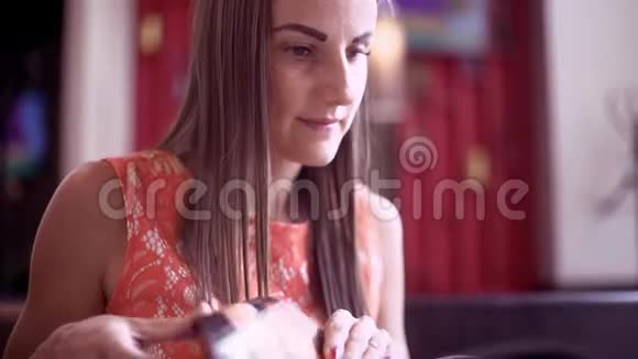 一个女人在咖啡馆里喝一杯冰沙翻阅菜单在电话上读信息并写下答案关闭视频的预览图