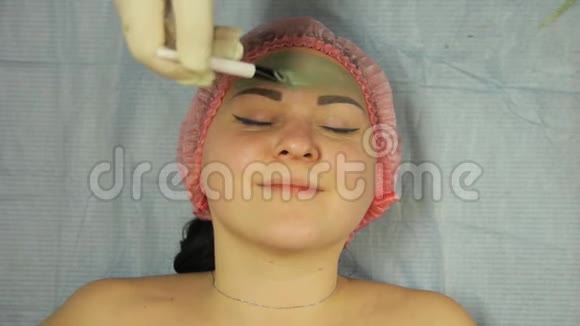 一位戴着手套的男性美容师用刷子在一位女性客户的脸上涂上一层泥面膜视频的预览图
