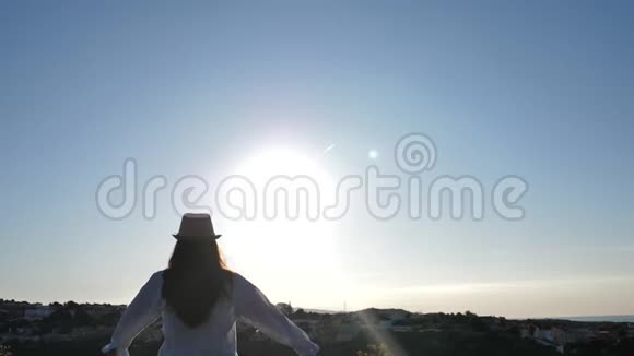 女人站在上面看着城市和大海在日落时举起双手向太阳看视频的预览图