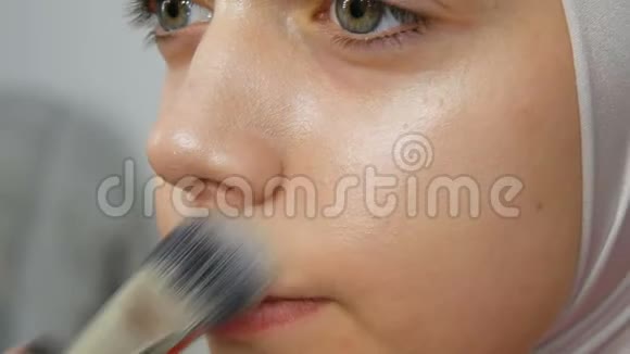 一个专业的化妆师用特殊的画笔将遮瑕膏应用于女孩模型高级时尚拍摄视频视频的预览图
