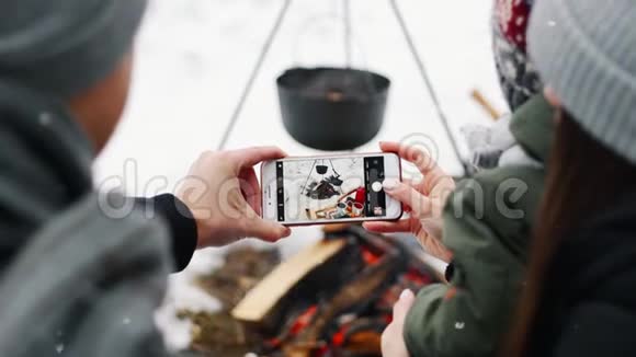 一对夫妇在冬季森林野餐时拍摄篝火视频的预览图