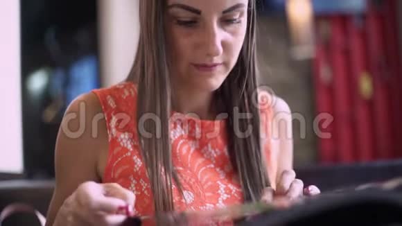 一个女人在咖啡馆里喝一杯冰沙翻阅菜单在电话上读信息并写下答案关闭视频的预览图