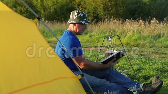 一个人在篝火帐篷附近看书看着沸腾的锅视频的预览图