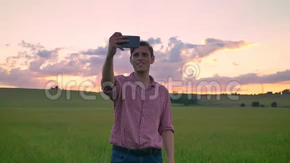 英俊的年轻人自拍站在小麦或黑麦田美丽的粉红色日落背景视频的预览图
