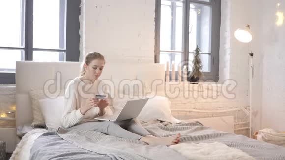 坐在床上为网上购物支付成功而兴奋的女孩视频的预览图