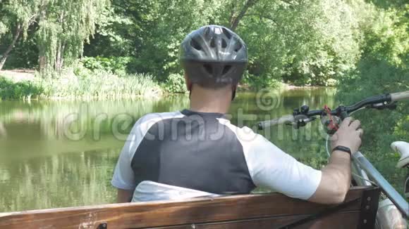 夏天一个骑自行车的人正在公园里休息他坐在池塘边的长凳上他戴着特殊的眼镜视频的预览图