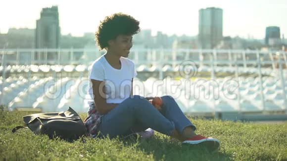 快乐的卷发女性吃新鲜苹果坐在绿色草坪上健康视频的预览图