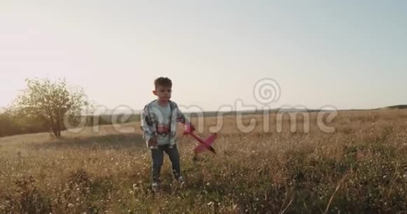 梦想着有魅力的小男孩玩着飞机在田野的中间跳跃缓慢的动作视频的预览图