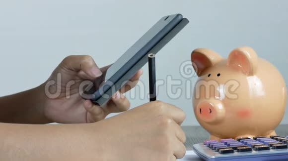 一个女人正在记笔记用一部智能手机把一滴钱放进一个存钱罐里视频的预览图