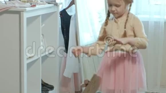 穿着粉红色裙子扎着辫子的开朗的小女孩穿着妈妈高跟鞋在镜子前跳舞视频的预览图